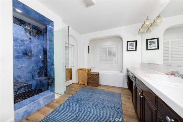 bathroom featuring a bath, a stall shower, wood finished floors, and vanity