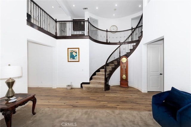 staircase with baseboards, a high ceiling, wood finished floors, and recessed lighting