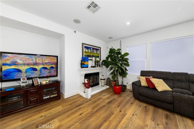 living area with recessed lighting, visible vents, a glass covered fireplace, wood finished floors, and baseboards