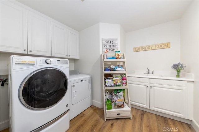 laundry area with cabinet space, baseboards, light wood-style floors, separate washer and dryer, and a sink