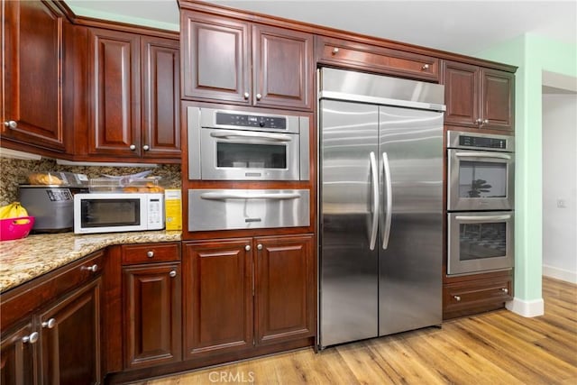 kitchen with a warming drawer, stainless steel appliances, backsplash, light wood-style floors, and light stone countertops