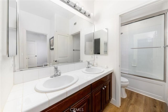 full bath featuring bath / shower combo with glass door, wood finished floors, a sink, and toilet