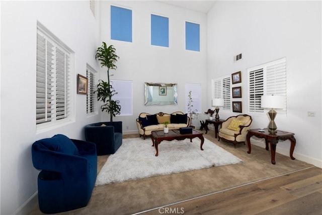 living room featuring a high ceiling, wood finished floors, visible vents, and baseboards