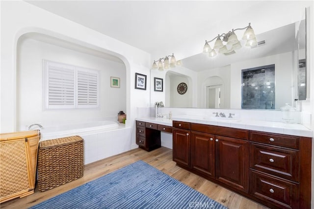 full bathroom with double vanity, visible vents, a sink, wood finished floors, and a bath