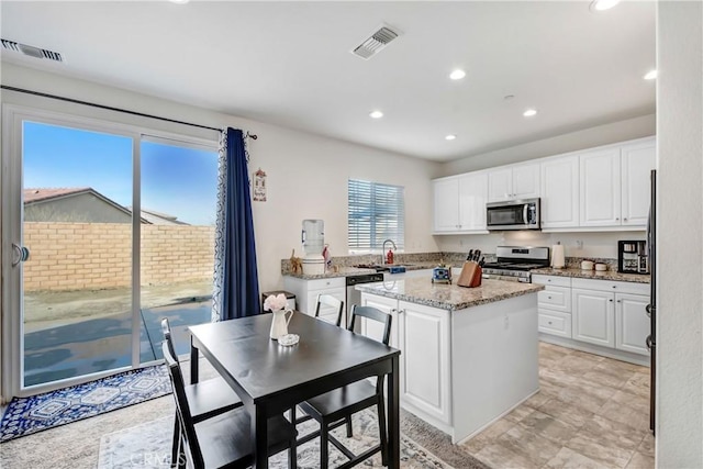 kitchen featuring sink, light stone counters, a kitchen island, stainless steel appliances, and white cabinets