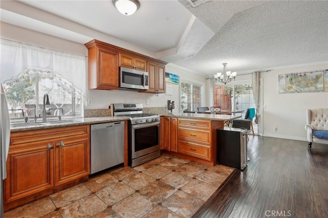 kitchen with pendant lighting, sink, appliances with stainless steel finishes, a notable chandelier, and kitchen peninsula