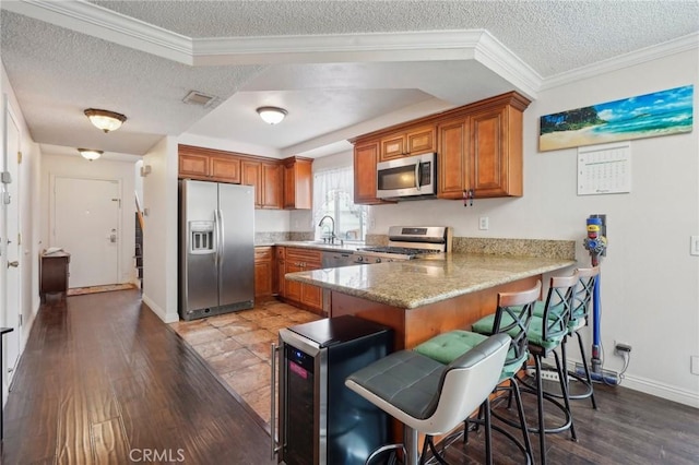 kitchen featuring a breakfast bar, sink, a textured ceiling, appliances with stainless steel finishes, and kitchen peninsula