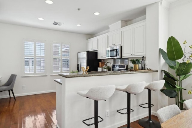 kitchen with appliances with stainless steel finishes, a kitchen breakfast bar, white cabinets, dark hardwood / wood-style flooring, and kitchen peninsula