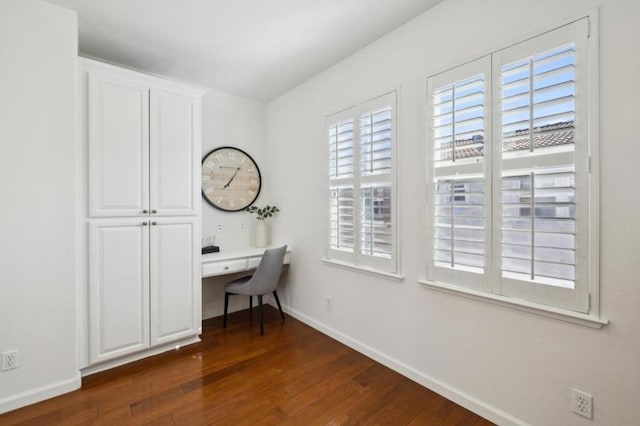 unfurnished office with built in desk, dark hardwood / wood-style floors, and a wealth of natural light