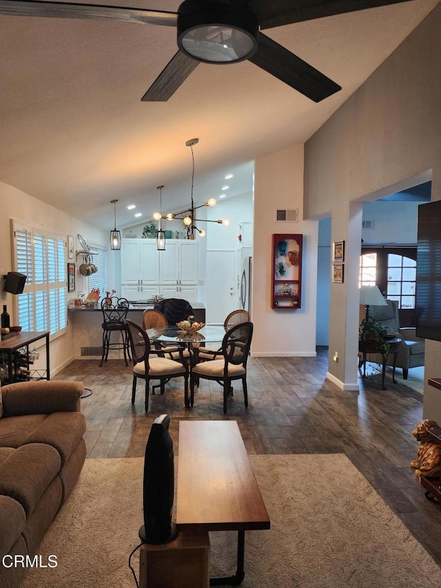 living room with ceiling fan with notable chandelier, a healthy amount of sunlight, dark hardwood / wood-style flooring, and vaulted ceiling