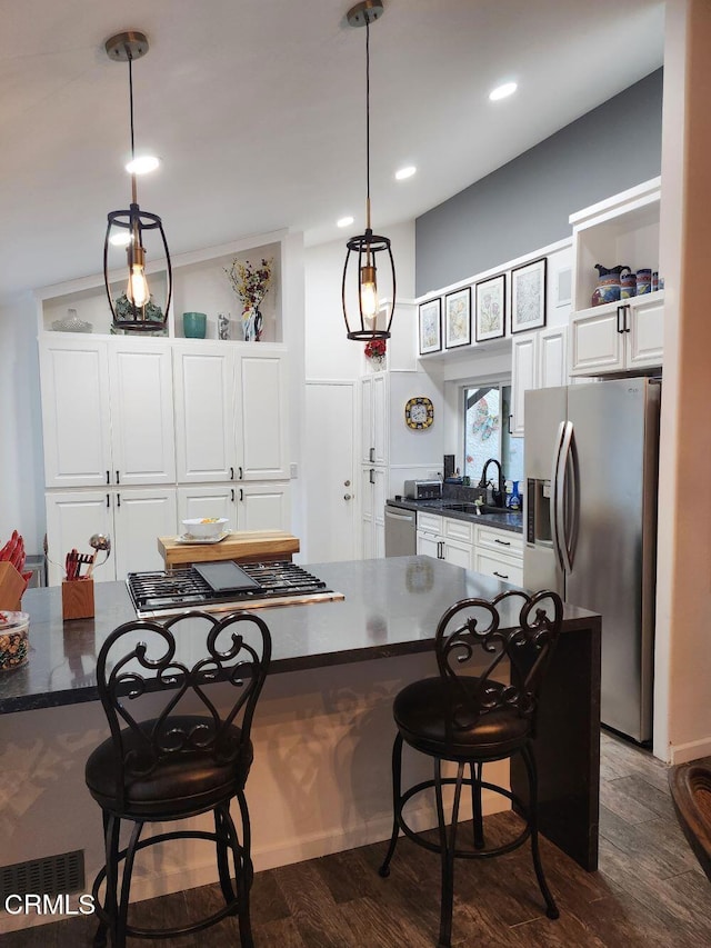 kitchen featuring dark wood-type flooring, a kitchen bar, hanging light fixtures, appliances with stainless steel finishes, and white cabinets