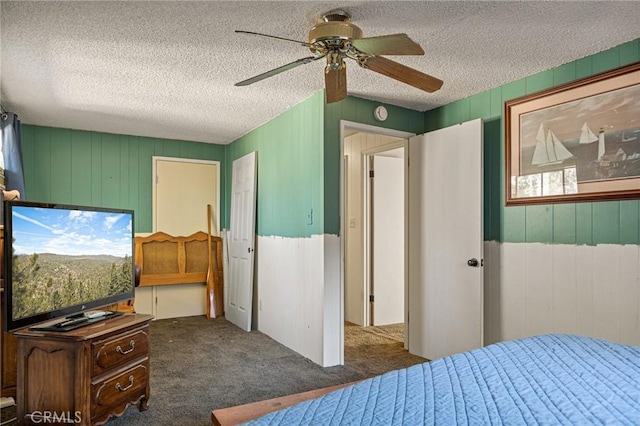 bedroom featuring dark colored carpet, wooden walls, a textured ceiling, and ceiling fan