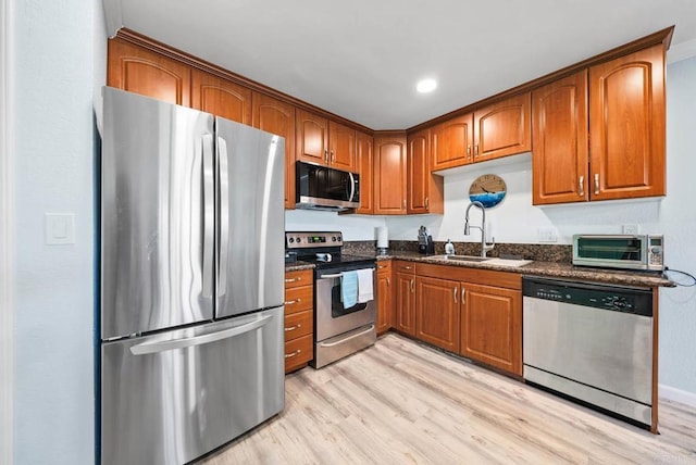 kitchen with dark stone countertops, sink, light wood-type flooring, and appliances with stainless steel finishes