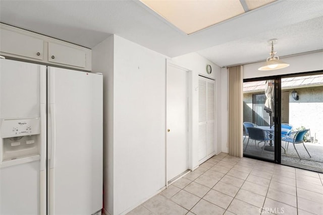 kitchen featuring pendant lighting, white refrigerator with ice dispenser, white cabinetry, and light tile patterned flooring