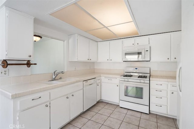 kitchen with sink, white appliances, light tile patterned floors, white cabinetry, and tile countertops