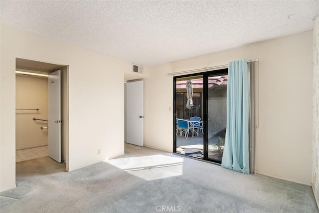 empty room featuring a textured ceiling, visible vents, and light colored carpet