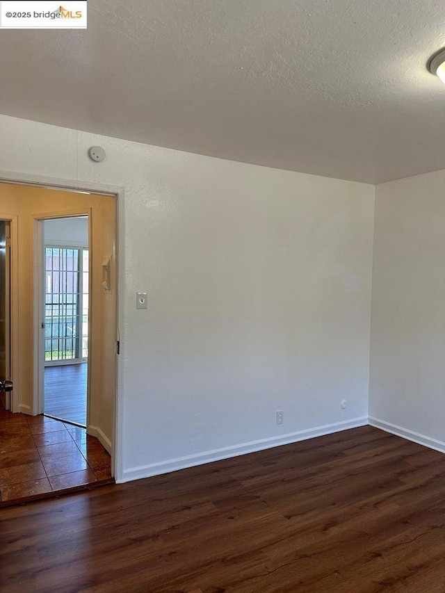 empty room with a textured ceiling and dark hardwood / wood-style flooring