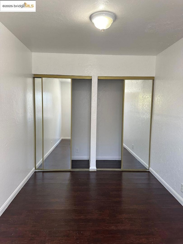 unfurnished bedroom with dark wood-type flooring and multiple closets