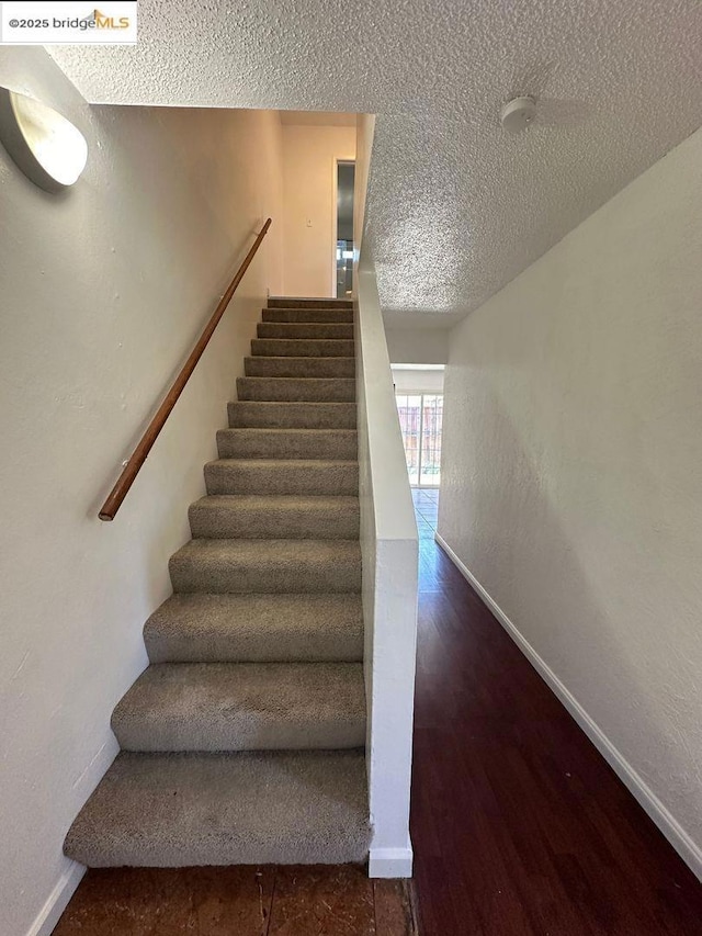 stairs with wood-type flooring and a textured ceiling