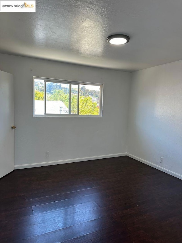 empty room with dark wood-type flooring and a textured ceiling