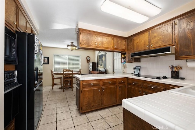 kitchen with light tile patterned floors, tasteful backsplash, black appliances, tile countertops, and kitchen peninsula