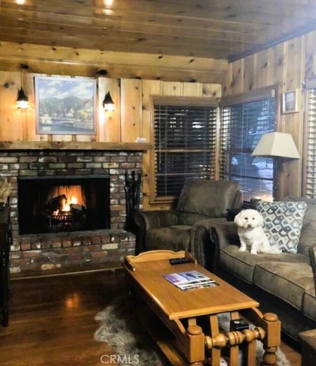 living room with dark wood-type flooring, wooden walls, and a fireplace