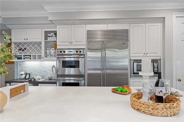 kitchen with tasteful backsplash, crown molding, built in appliances, and white cabinets