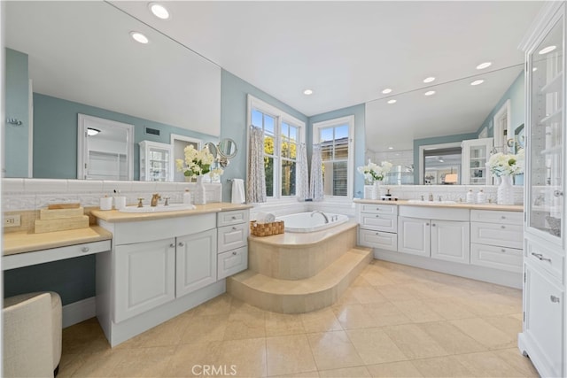 bathroom featuring tile patterned flooring, backsplash, vanity, and tiled bath