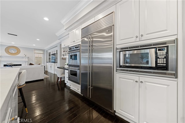 kitchen with ornamental molding, stainless steel appliances, dark hardwood / wood-style floors, and white cabinets