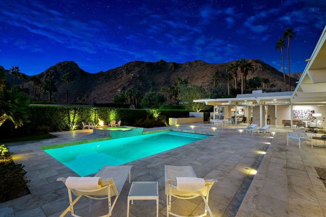 pool at night featuring a mountain view, a patio area, and an in ground hot tub