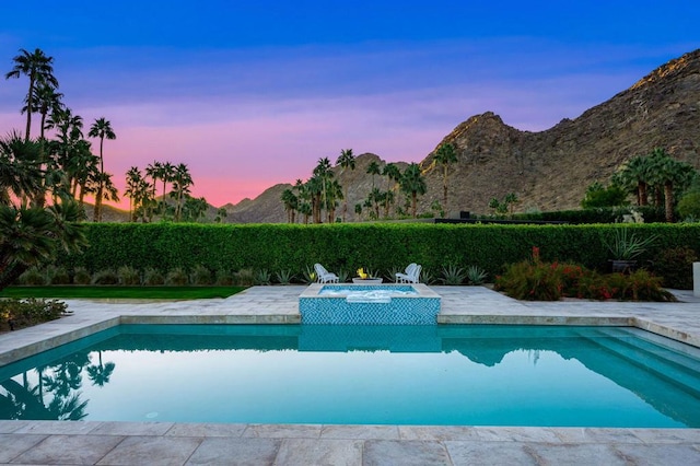 pool at dusk with an in ground hot tub and a mountain view