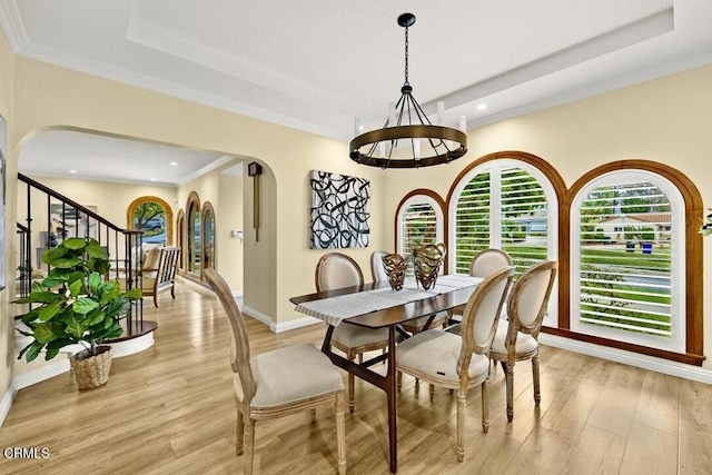 dining room featuring a raised ceiling, ornamental molding, and light hardwood / wood-style flooring