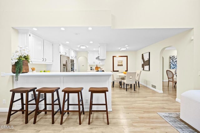 kitchen featuring a breakfast bar area, stainless steel fridge, white cabinetry, kitchen peninsula, and light wood-type flooring