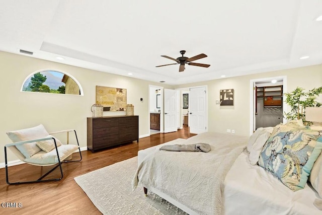 bedroom featuring a raised ceiling, ensuite bathroom, hardwood / wood-style floors, and ceiling fan