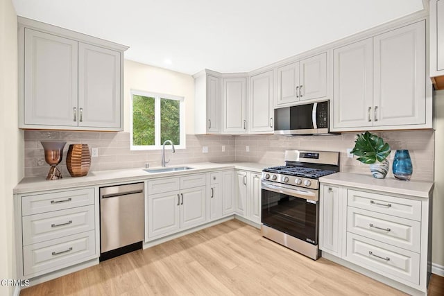 kitchen featuring sink, light hardwood / wood-style flooring, white cabinetry, backsplash, and stainless steel appliances