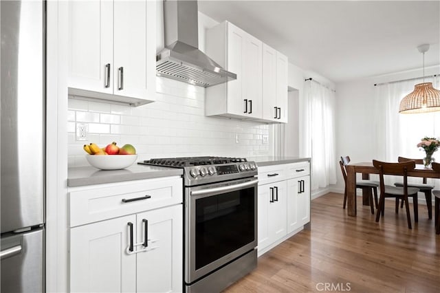 kitchen with hanging light fixtures, white cabinetry, appliances with stainless steel finishes, and wall chimney range hood