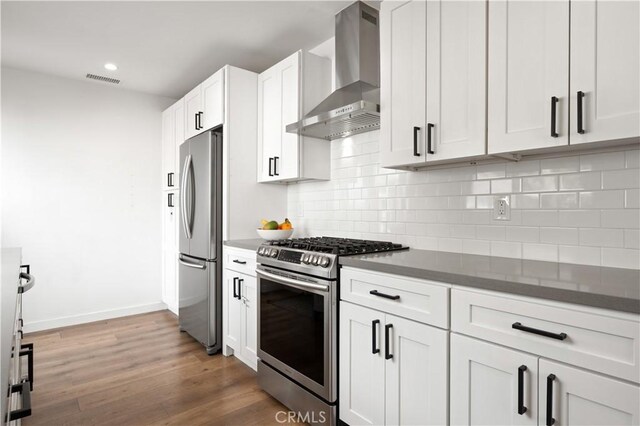 kitchen with dark wood-type flooring, white cabinetry, wall chimney range hood, stainless steel appliances, and backsplash