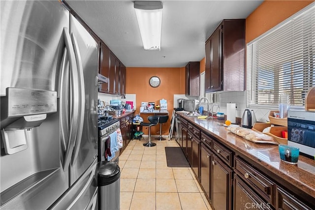 kitchen with stainless steel refrigerator with ice dispenser, sink, light tile patterned floors, dark stone counters, and decorative backsplash