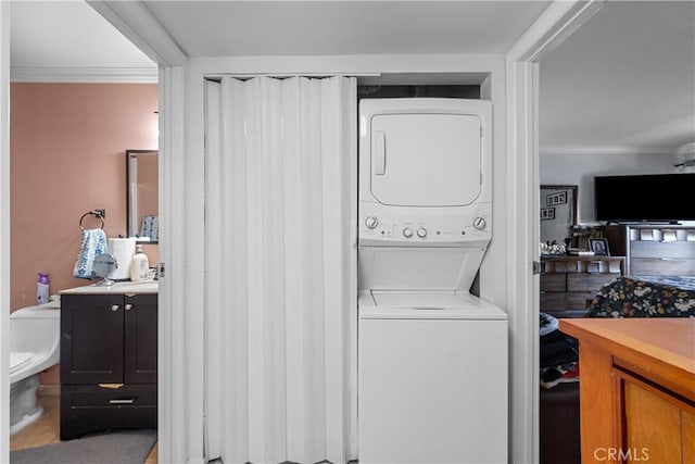 washroom with ornamental molding, stacked washer and clothes dryer, and tile patterned floors