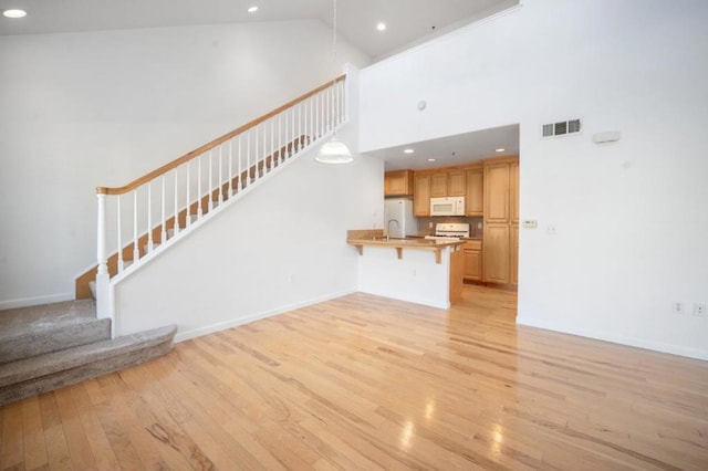 unfurnished living room featuring light wood-type flooring, sink, and high vaulted ceiling