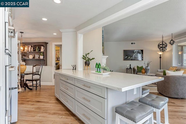 kitchen featuring a breakfast bar area, hanging light fixtures, light wood-type flooring, a kitchen island, and white cabinets