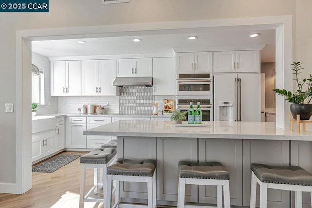 kitchen featuring white cabinetry, high end refrigerator, a kitchen bar, and white double oven