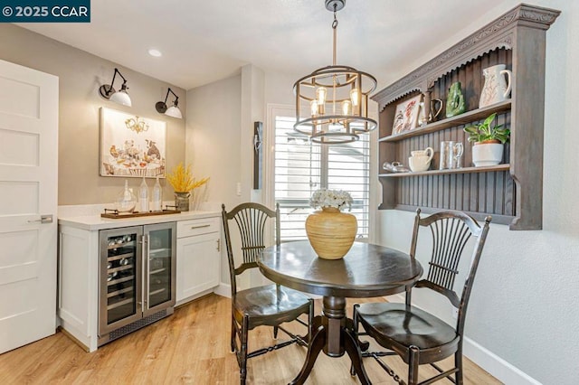 dining room featuring wine cooler, indoor bar, light hardwood / wood-style floors, and an inviting chandelier