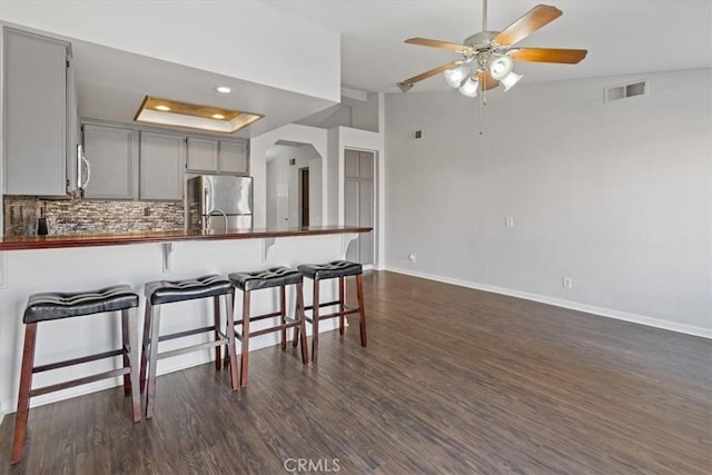 kitchen featuring dark wood-type flooring, a kitchen breakfast bar, gray cabinets, stainless steel appliances, and backsplash