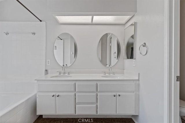 bathroom featuring toilet, vanity, and tiled bath