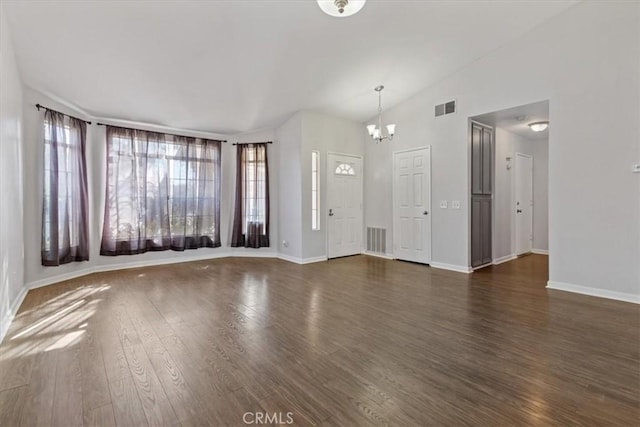 unfurnished living room with vaulted ceiling, dark hardwood / wood-style floors, a wealth of natural light, and a notable chandelier