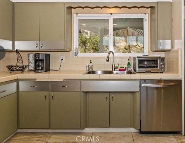 kitchen with sink, green cabinets, backsplash, tile countertops, and stainless steel dishwasher