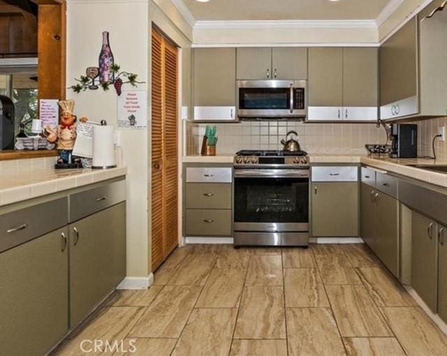 kitchen featuring tasteful backsplash, ornamental molding, stainless steel appliances, and tile countertops