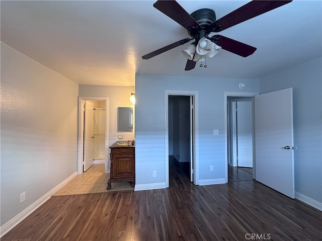 unfurnished bedroom featuring dark wood-type flooring, ensuite bathroom, a spacious closet, a closet, and ceiling fan