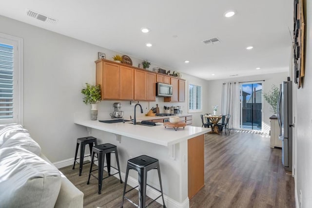 kitchen featuring a kitchen bar, sink, dark hardwood / wood-style floors, kitchen peninsula, and stainless steel appliances